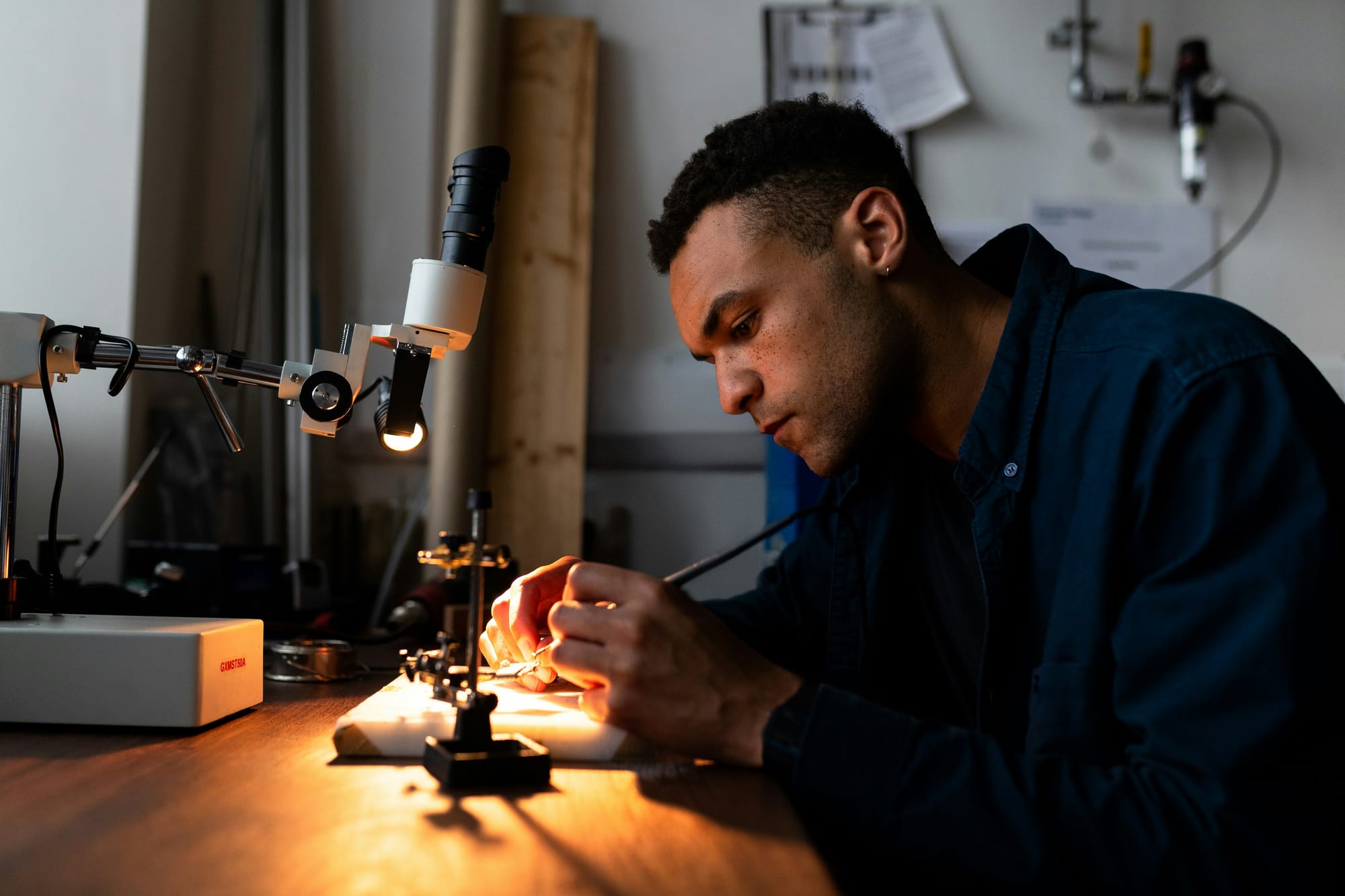 Técnico soldando componentes SMD sob microscópio de bancada com iluminação lateral quente
